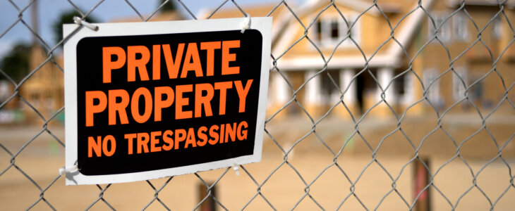 A "No Trespassing" sign and chain link fence with a large out of focus home under construction in the background.