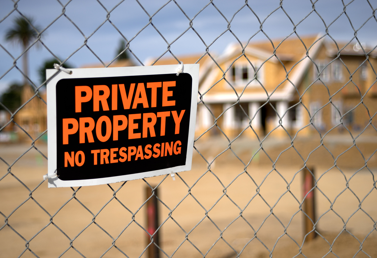 A "No Trespassing" sign and chain link fence with a large out of focus home under construction in the background.