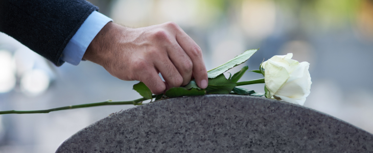 man placing a white rose on top of a tombstone