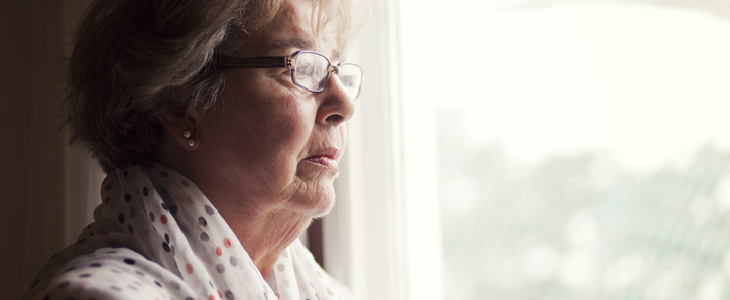 Elderly woman looking out of her window in sorrow