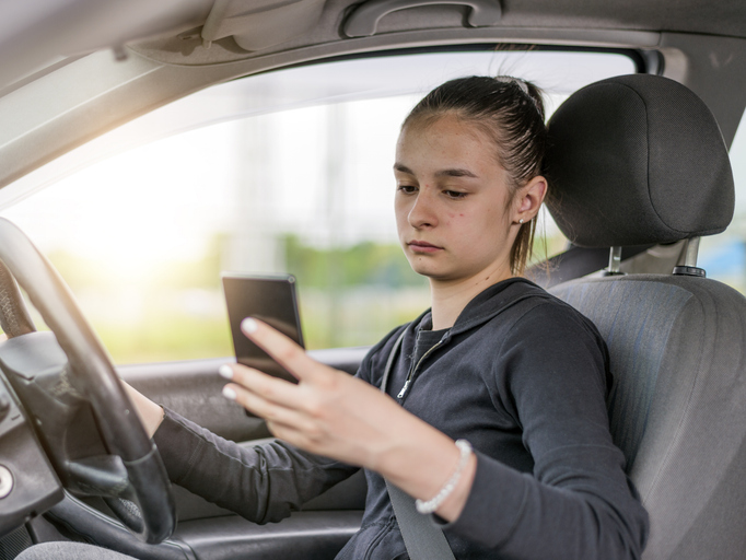 Young female student driver texting while driving.