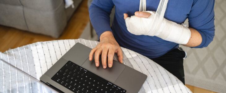 Adult man, using a laptop while having a hand in the orthopedic cast