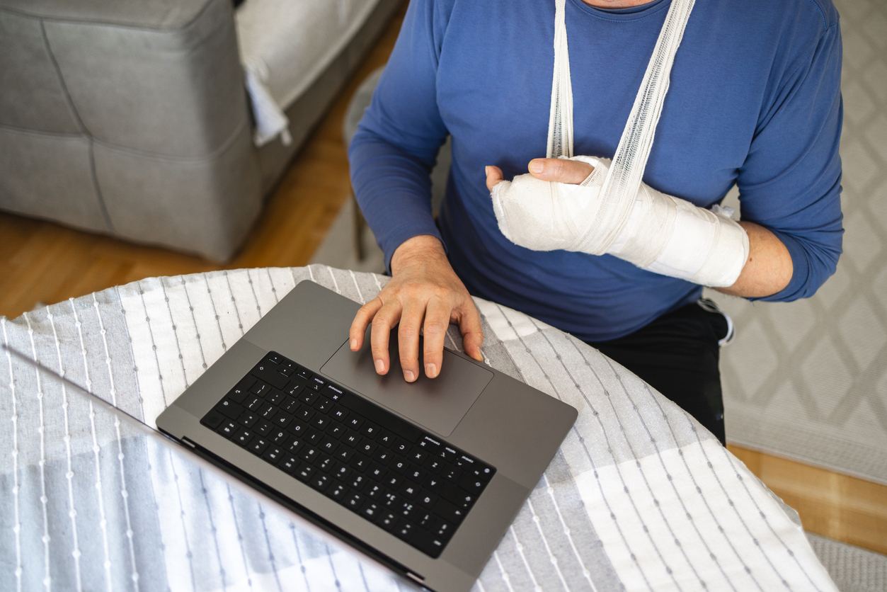 Adult man, using a laptop while having a hand in the orthopedic cast