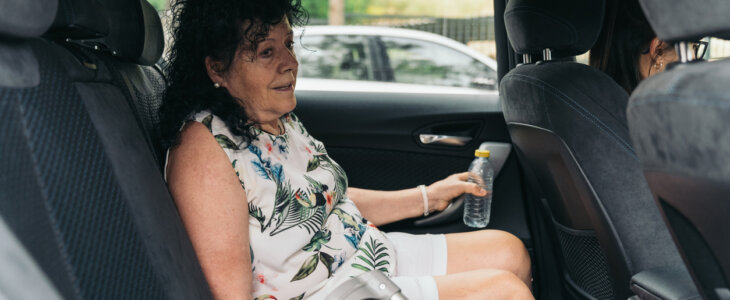 Elderly woman is traveling by taxi, holding her walking stick while sitting in the back seat.